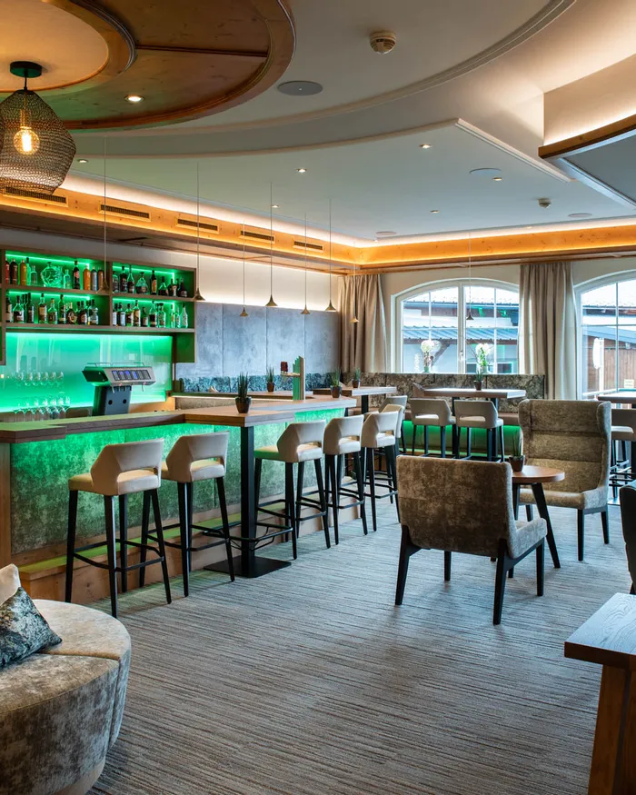Moderne Hotelbar mit grüner LED-Beleuchtung, Barhockern und gemütlichen Lounge-Sesseln